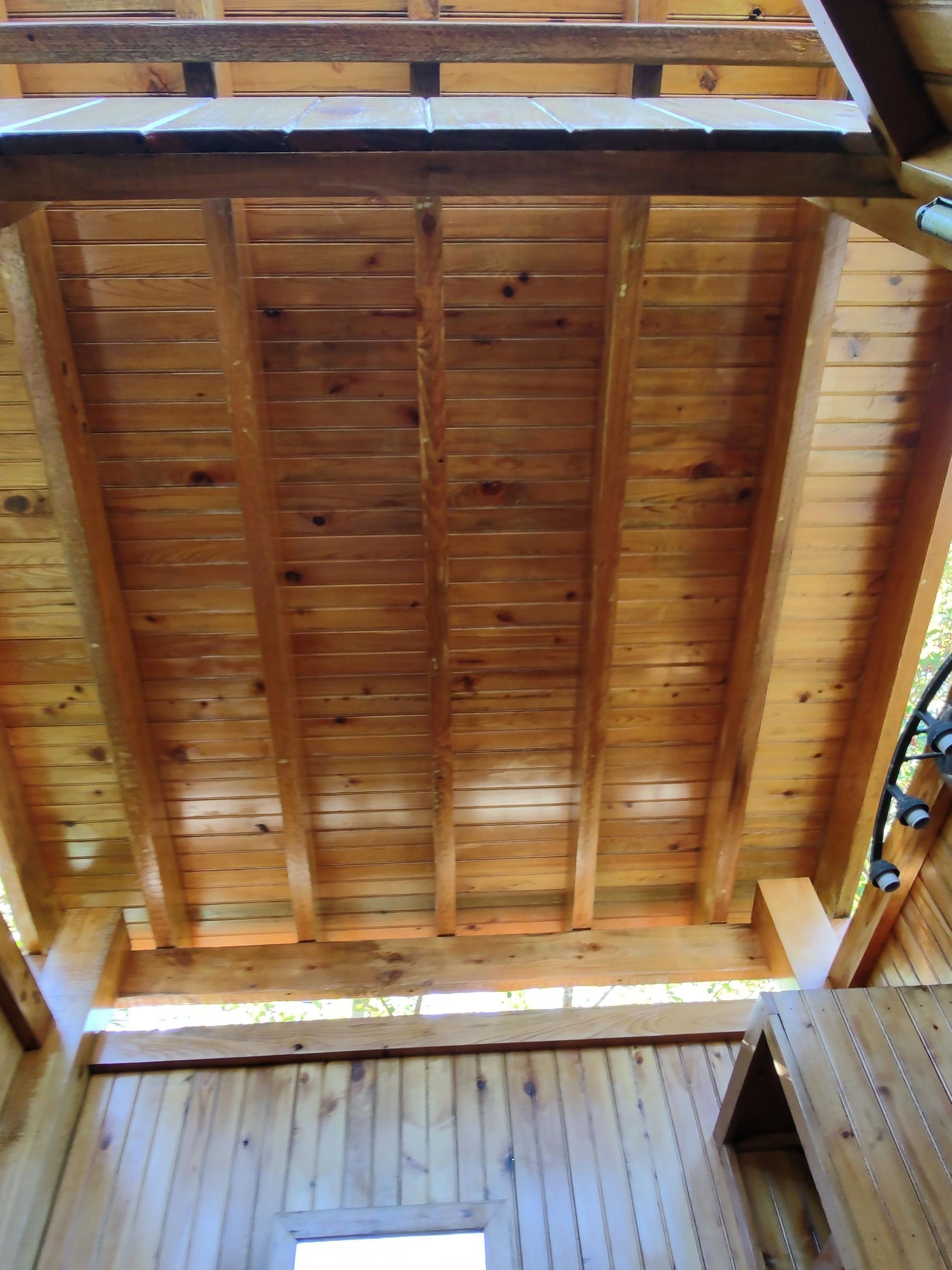 Looking up at the ceiling of a wooden house with a window.