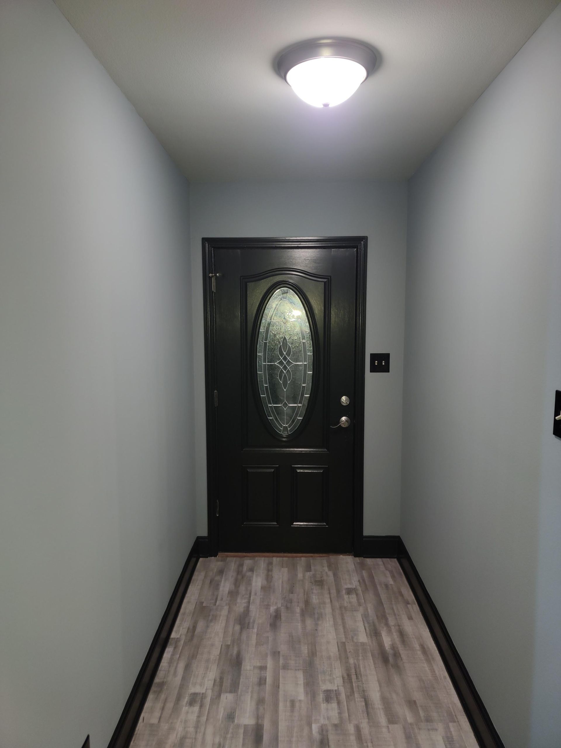 A hallway with a black door and a light on the ceiling.