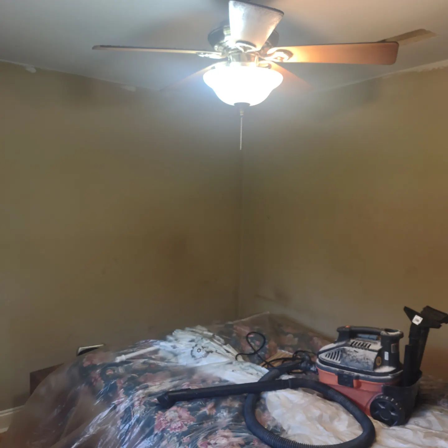 A bedroom with a ceiling fan and a vacuum cleaner on the bed