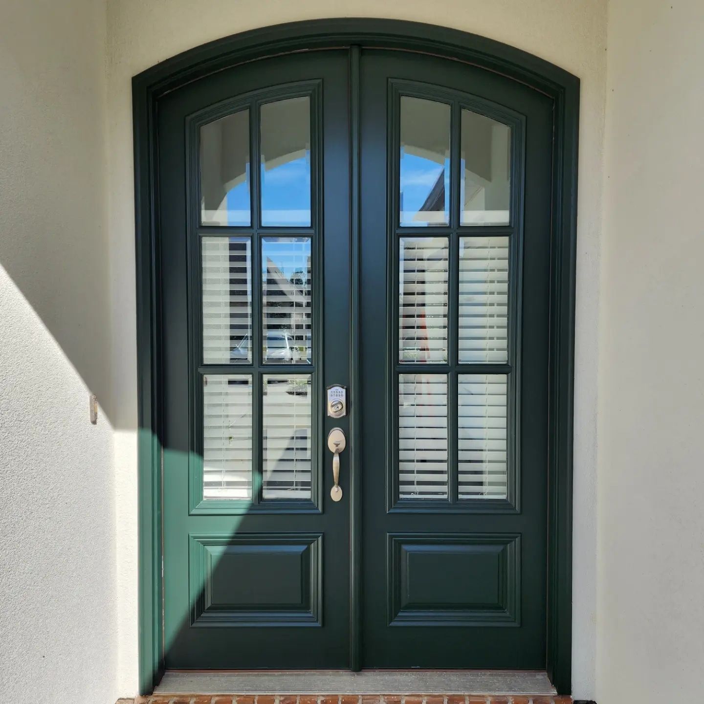 A green double door with arched windows on a white wall.
