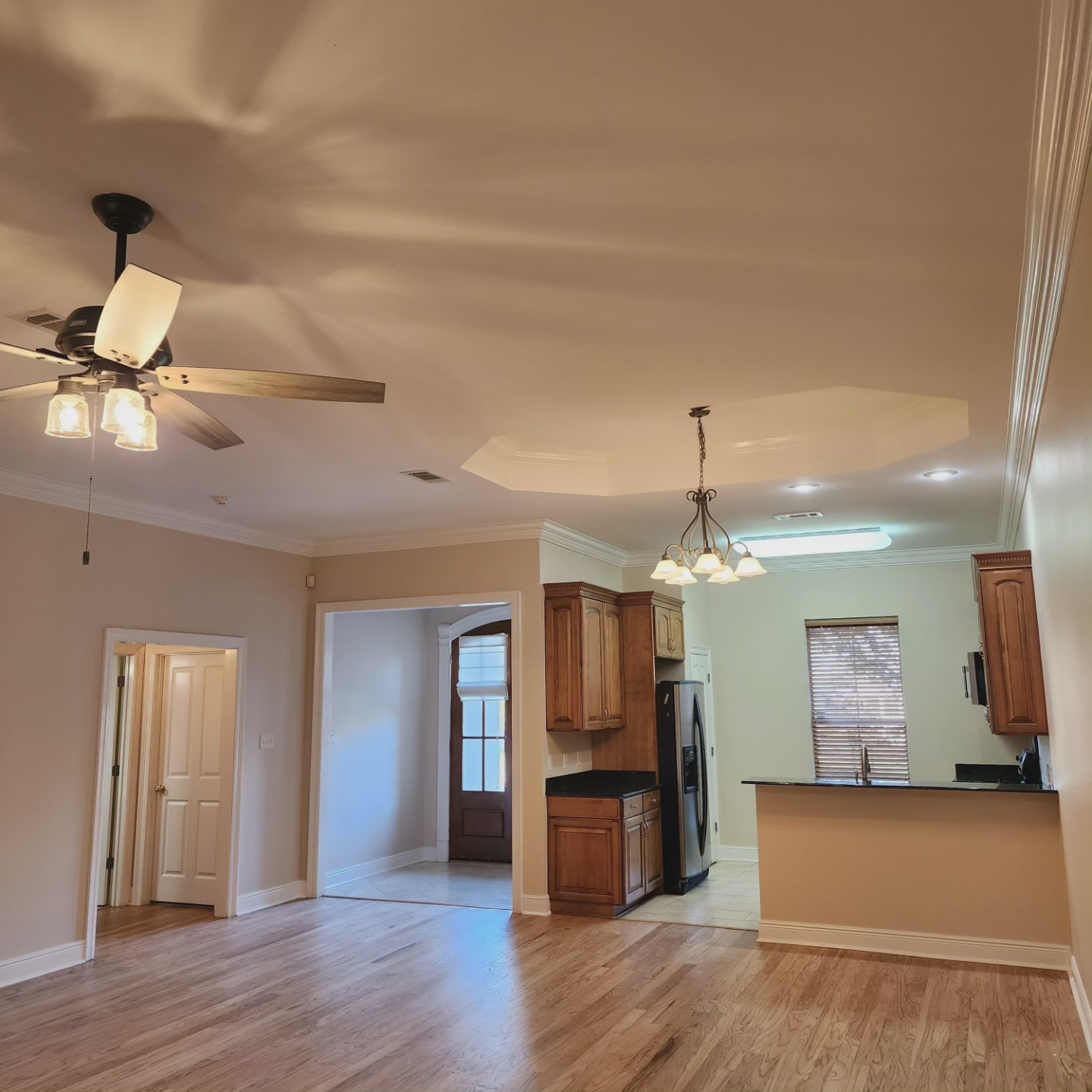 A living room with a ceiling fan and a kitchen in the background