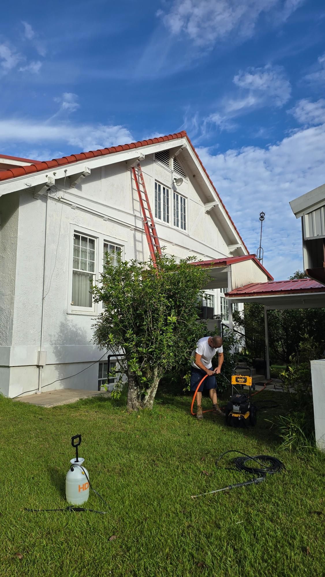 A man is standing in front of a white house with a red roof.