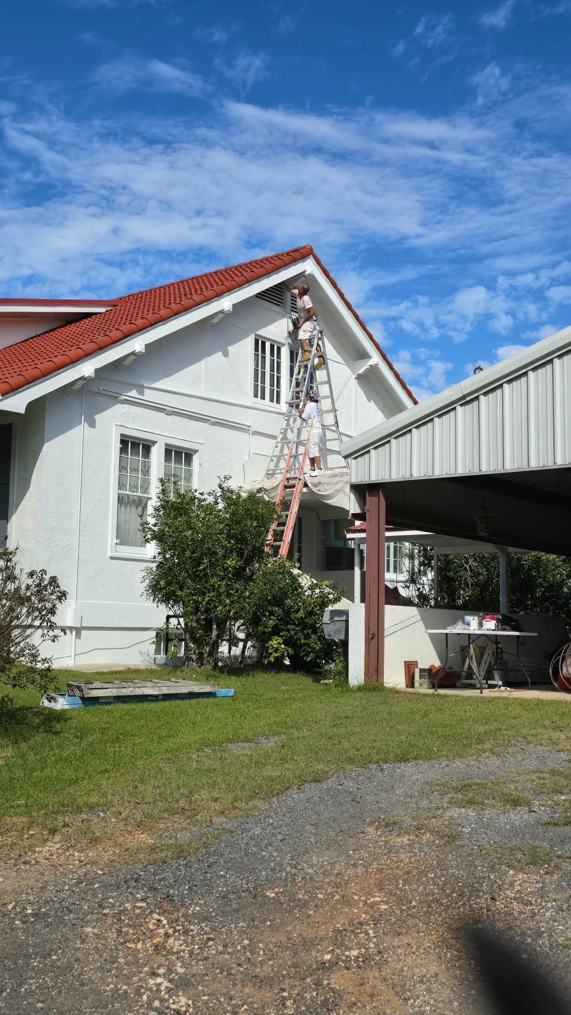 A man is painting a white house with a red roof.