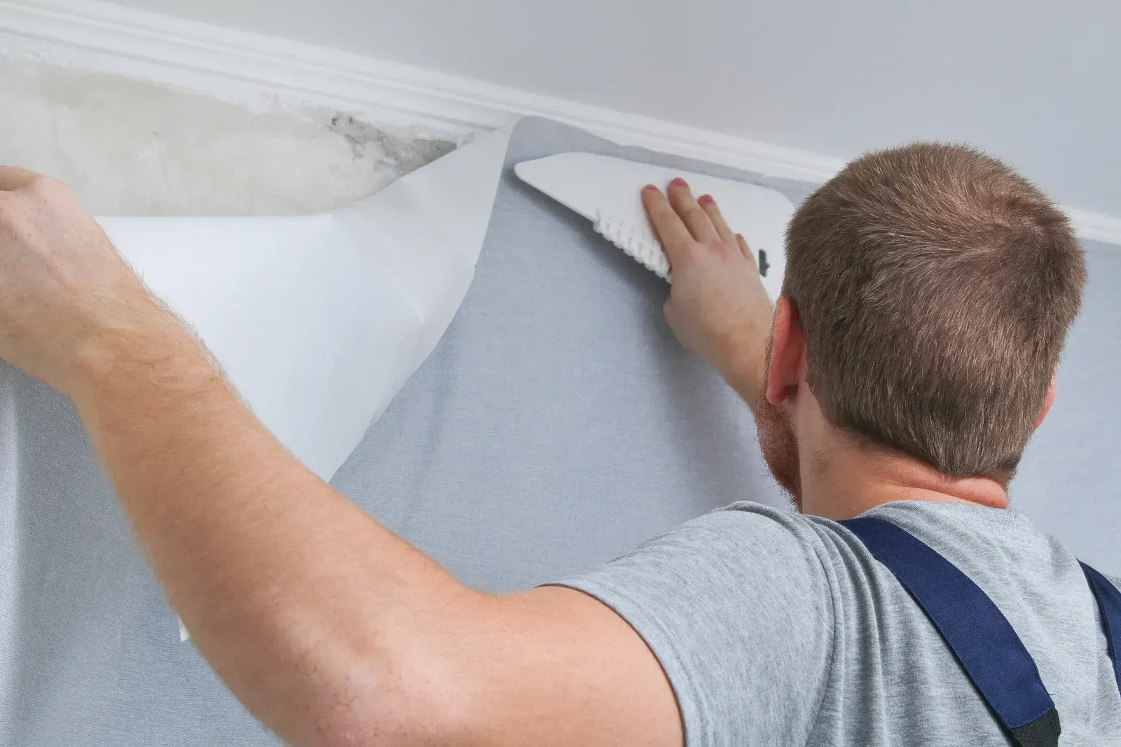 A man is applying wallpaper to a wall with a spatula.