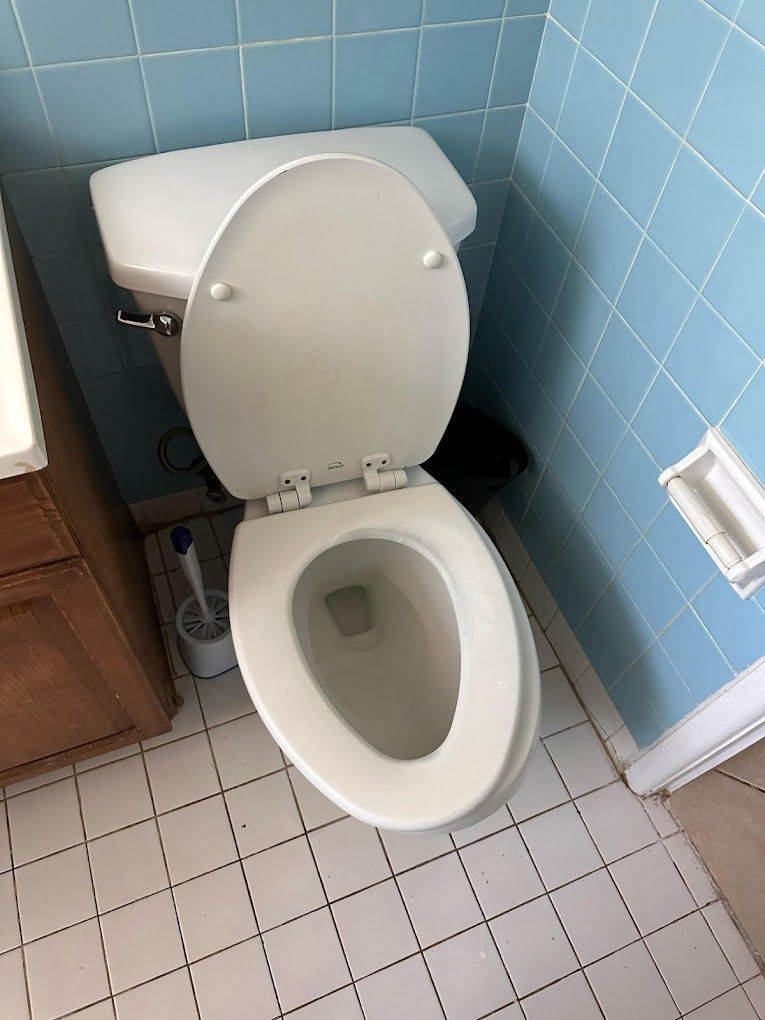 A toilet in a bathroom with blue tiles and a toilet brush.