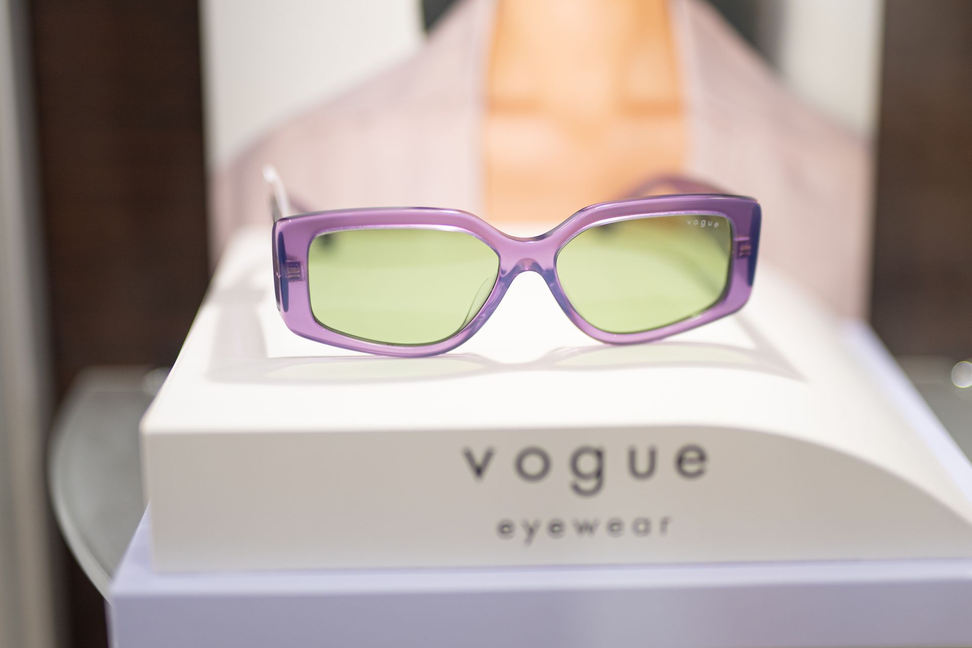 Occhiali da sole Vogue viola con lenti verdi su sfondo bianco.
