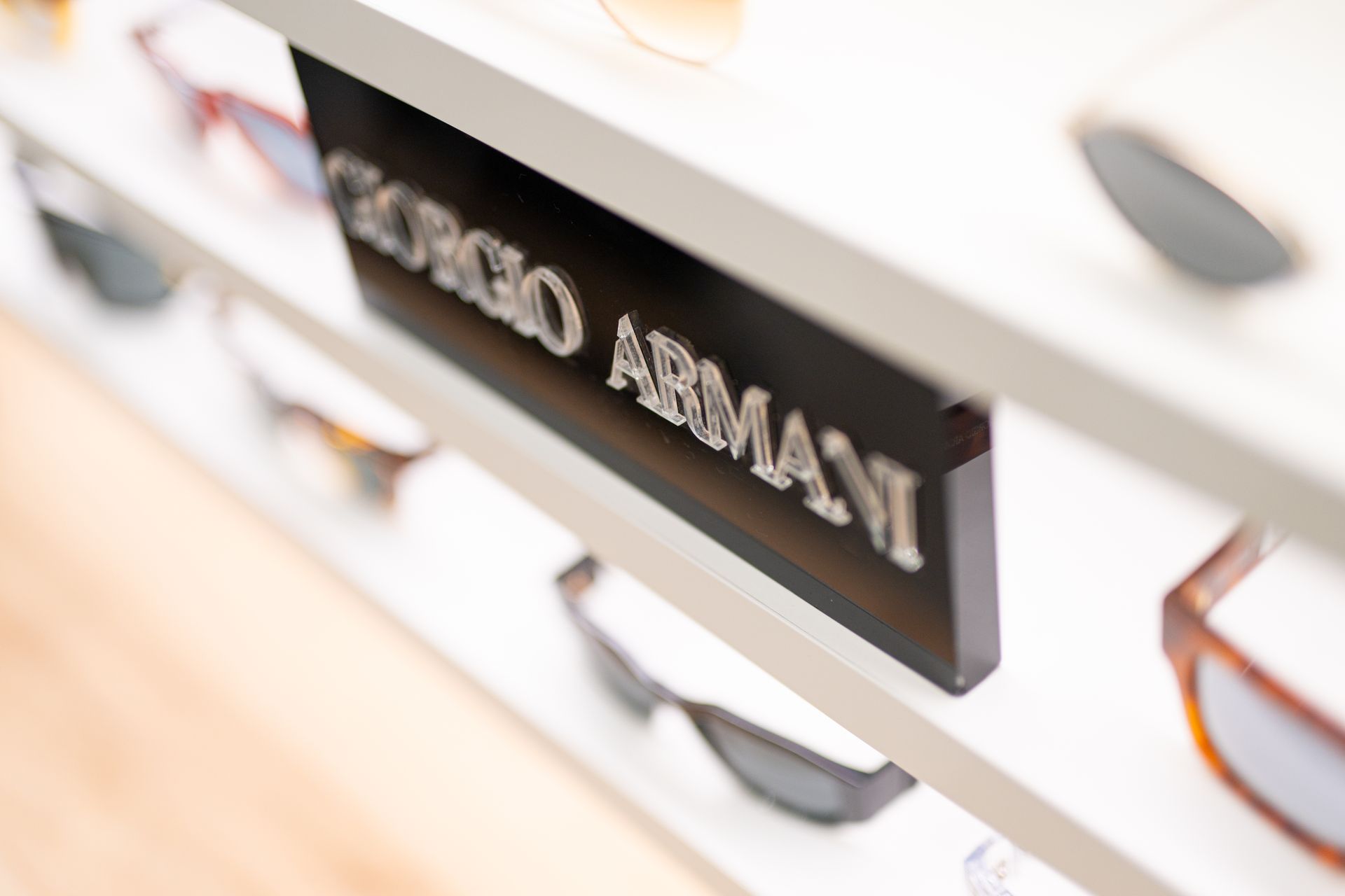 Occhiali da sole Giorgio Armani esposti su scaffali bianchi con un'insegna nera.
