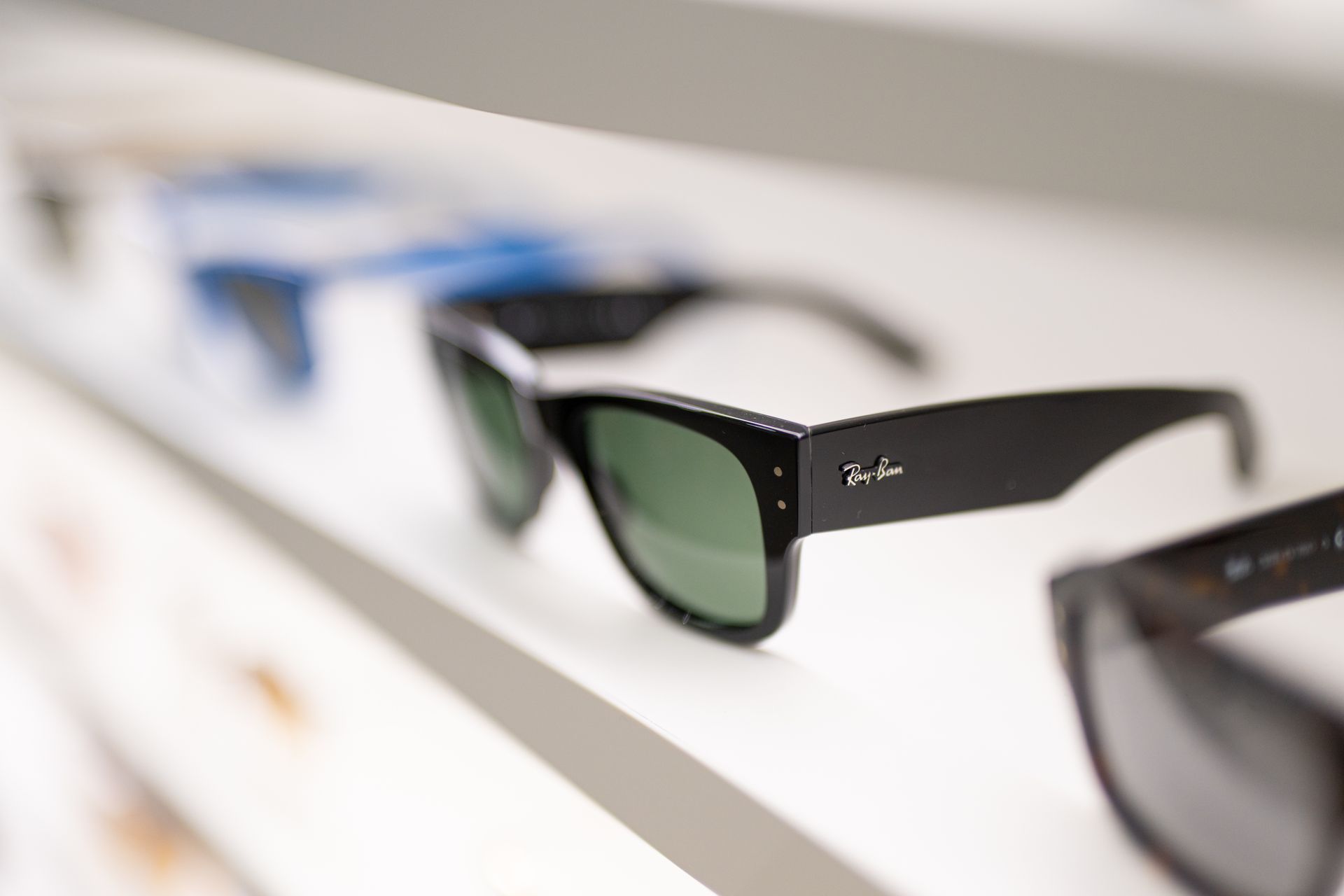 Occhiali da sole Ray-Ban neri su uno scaffale, altri occhiali da sole sullo sfondo.