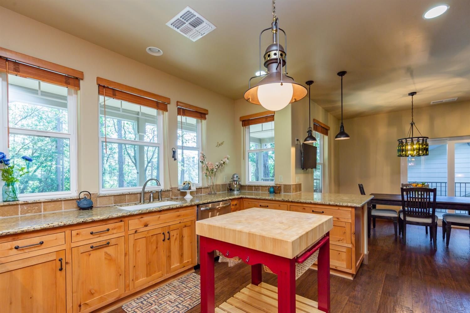 A kitchen with wooden cabinets , granite counter tops , a red table and a sink.