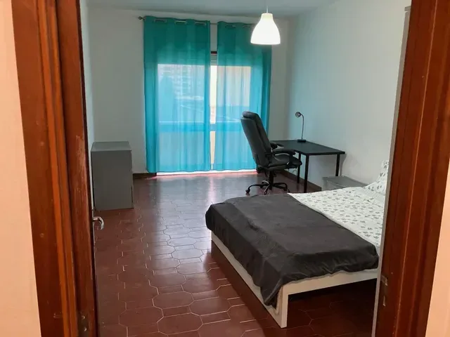 A bedroom with a bed , desk , chair and blue curtains.