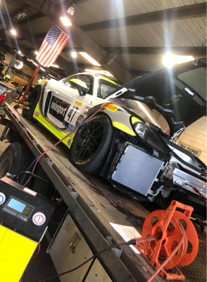 Race car on a tow truck, partially disassembled. White, black, and yellow paint. American flag in the background. | Allen's Automotive Service