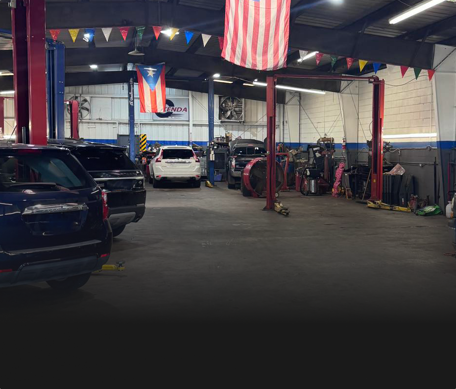 Interior of a busy auto repair shop with several cars on lifts and American and Puerto Rican flags hanging. | Allen's Automotive Service