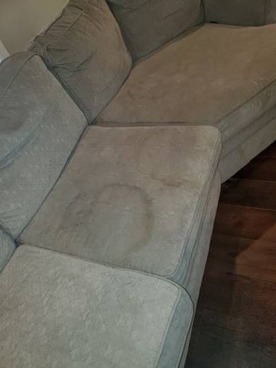 A couch with stains on it is sitting on a wooden floor in a living room.