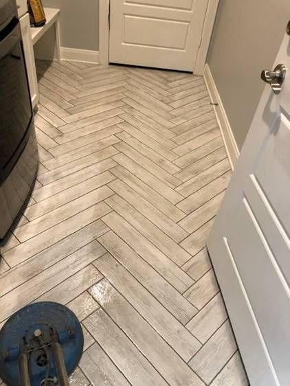 A herringbone tile floor in a laundry room next to a door.