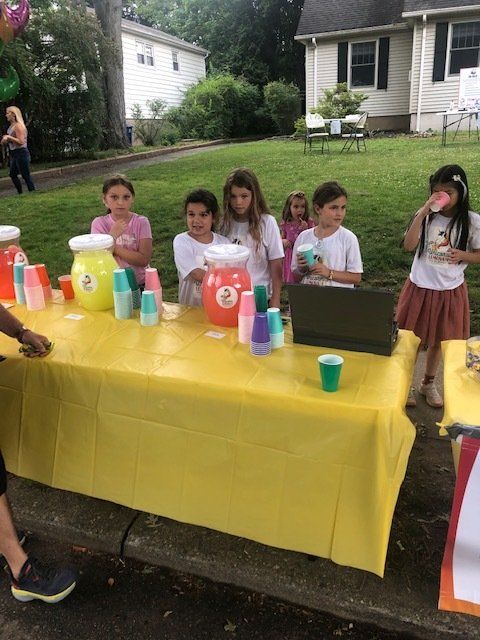 A group of children are standing around a table selling lemonade.