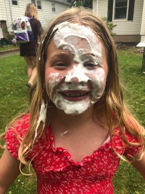 A little girl with shaving cream on her face is smiling.