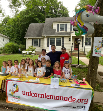 A group of people standing around a table that says unicornlemonade.org