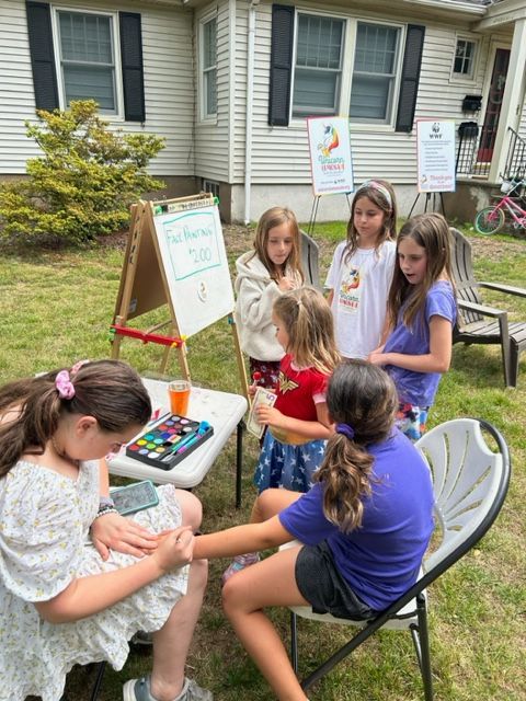 A group of young girls are sitting around a table in front of a house.