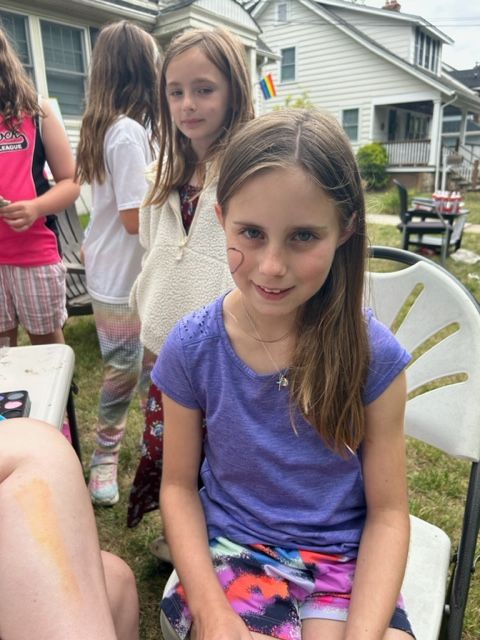 A girl with a cat face painted on her face is sitting in a chair