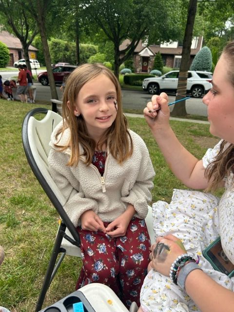 A little girl is getting her face painted by a woman.