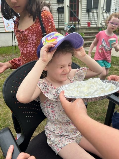 A little girl wearing a hat is holding a plate of food on her head