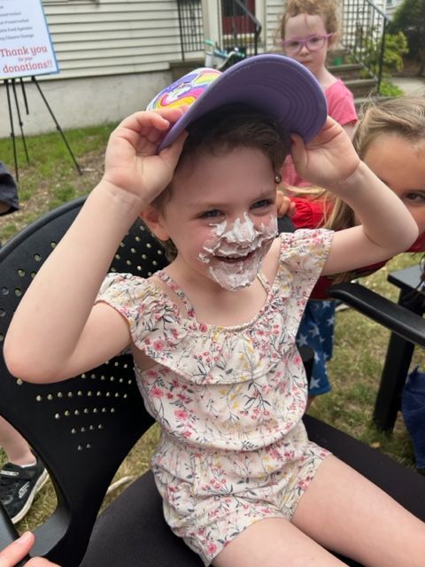 A little girl with frosting on her face is wearing a hat