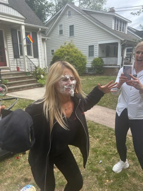 A woman with cake on her face is standing in front of a house.