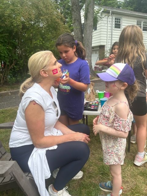 A woman is getting her face painted by a little girl.