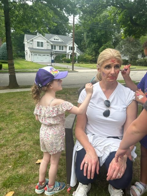 A little girl is painting a woman 's face in a park.