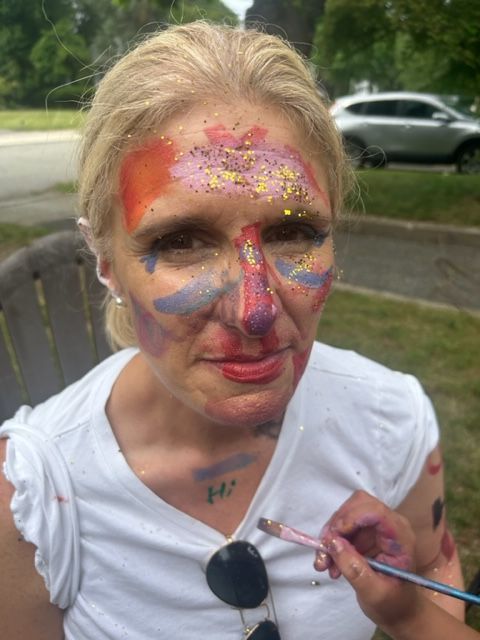 A woman is getting her face painted with a brush.