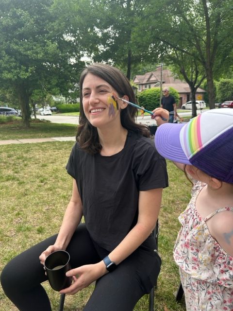 A woman is getting her face painted by a little girl.