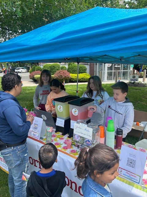 A group of children are standing around a table under a blue tent.