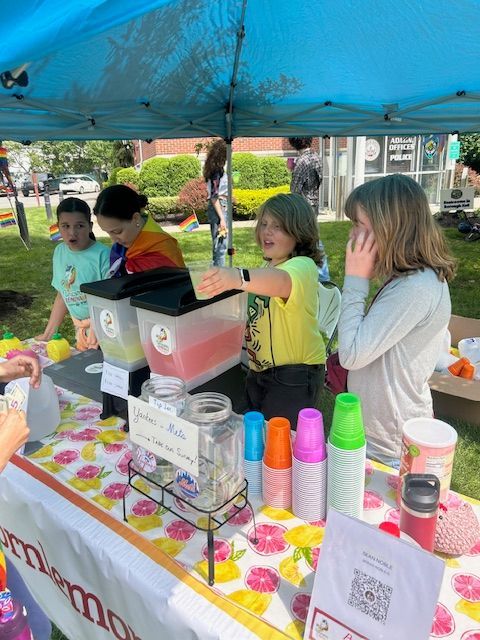 A group of children are standing around a table selling drinks.