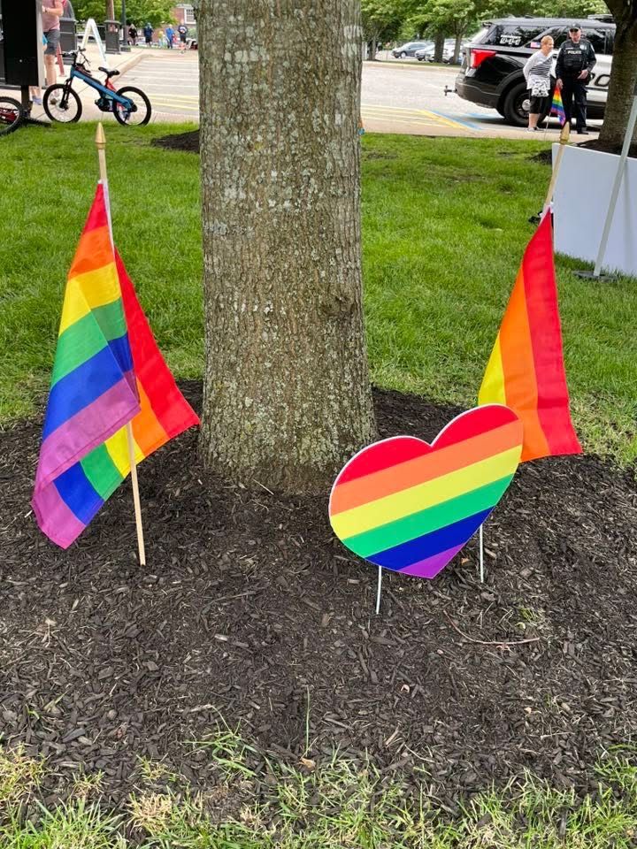 Two rainbow flags and a heart shaped rainbow flag are sitting next to a tree.