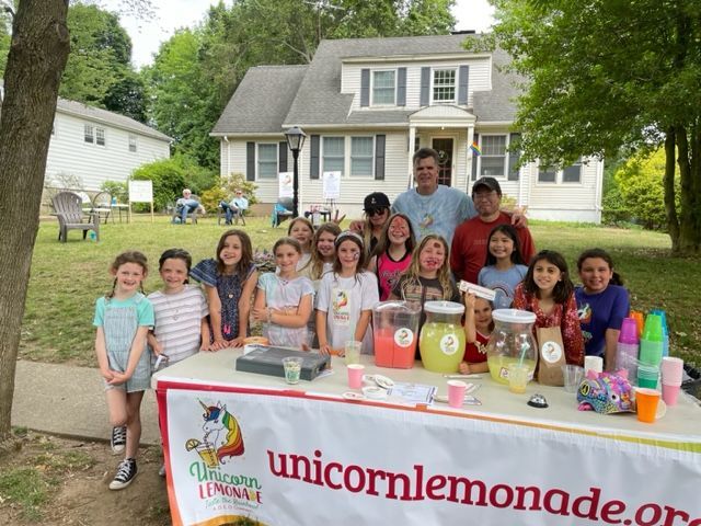 A group of children standing around a table that says unicorn lemonade