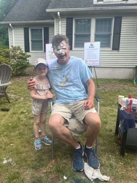 A man is sitting in a chair with his face painted and a little girl is standing next to him.
