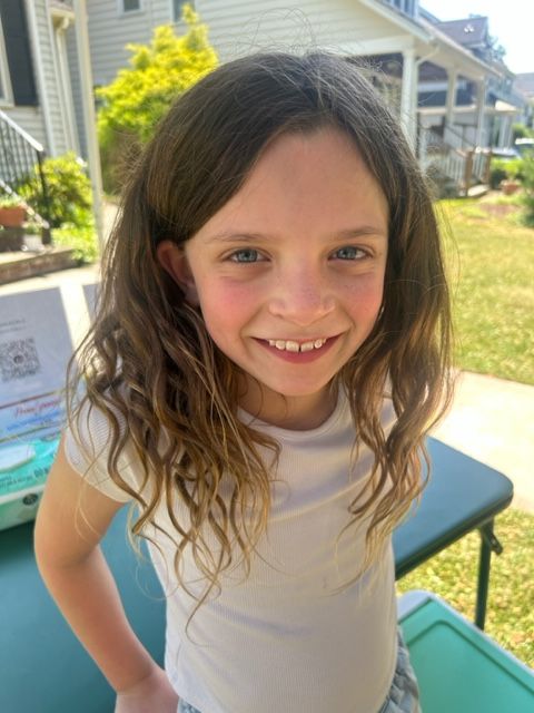 A little girl is smiling for the camera while standing in front of a table.
