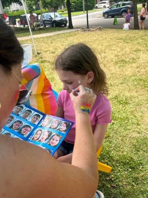 A woman is painting a little girl 's face in a park.
