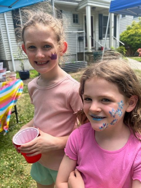 Two young girls with paint on their faces are standing next to each other.
