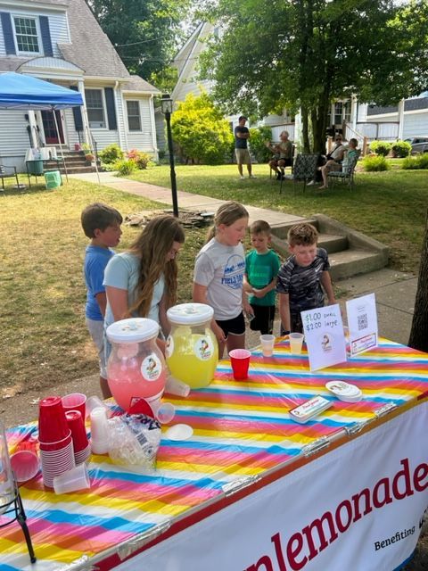 A group of children standing around a table that says lemonade