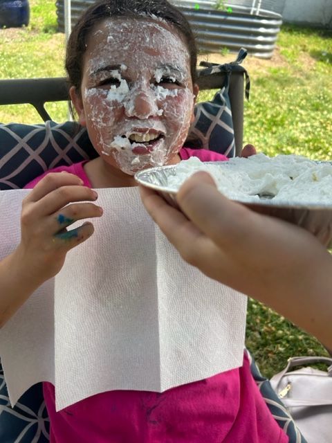 A girl with icing on her face is holding a paper towel and a plate of food