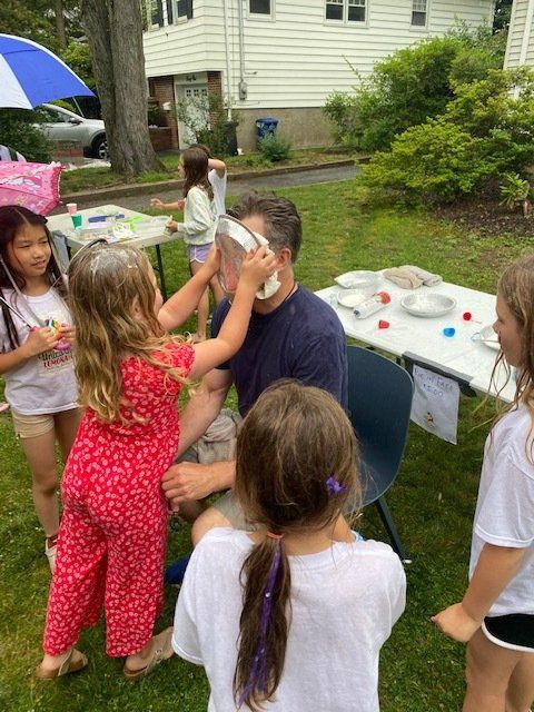 A group of children are playing with a man in a yard.