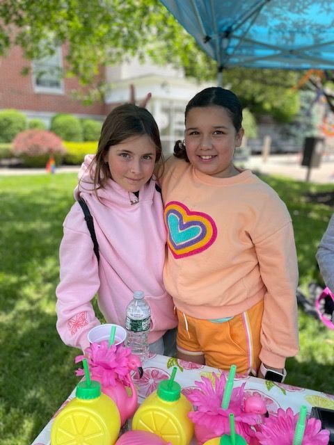 Two young girls are standing next to each other at a table.
