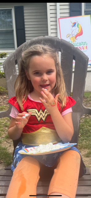 A little girl in a wonder woman costume is sitting in a chair eating marshmallows.