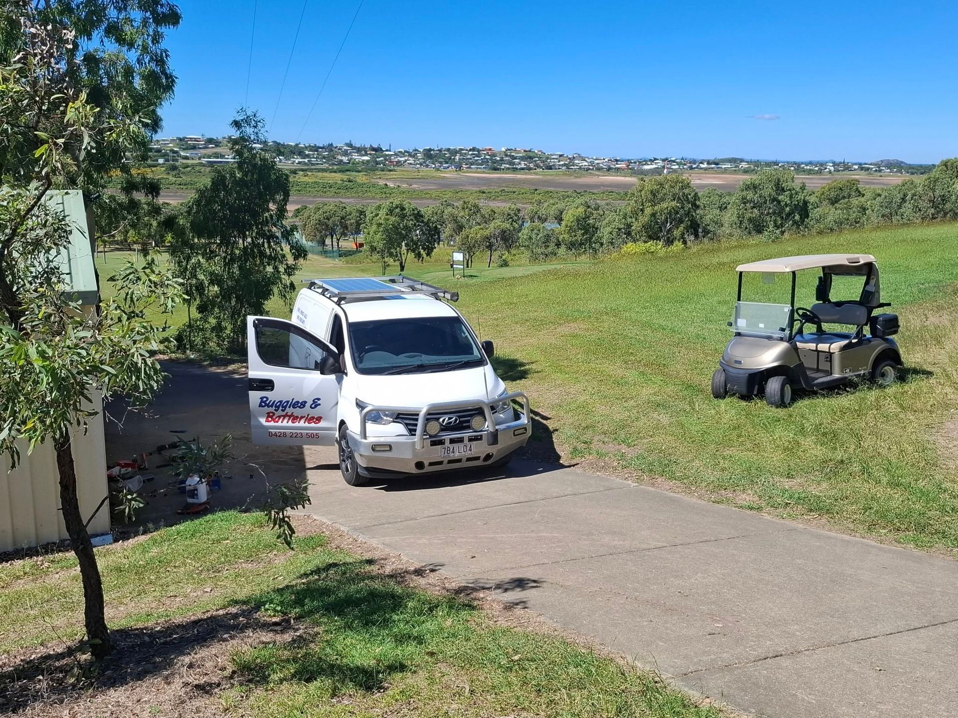 White Van With Open Door Next to a Golf Cart on a Grassy Hill — Buggies & Batteries in Moranbah, QLD