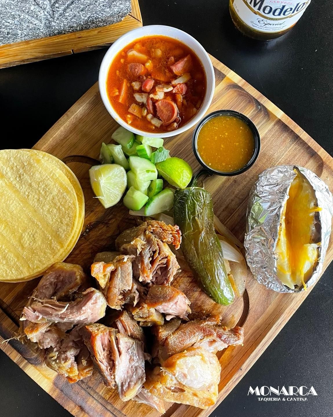 A wooden cutting board topped with meat , vegetables and a baked potato.