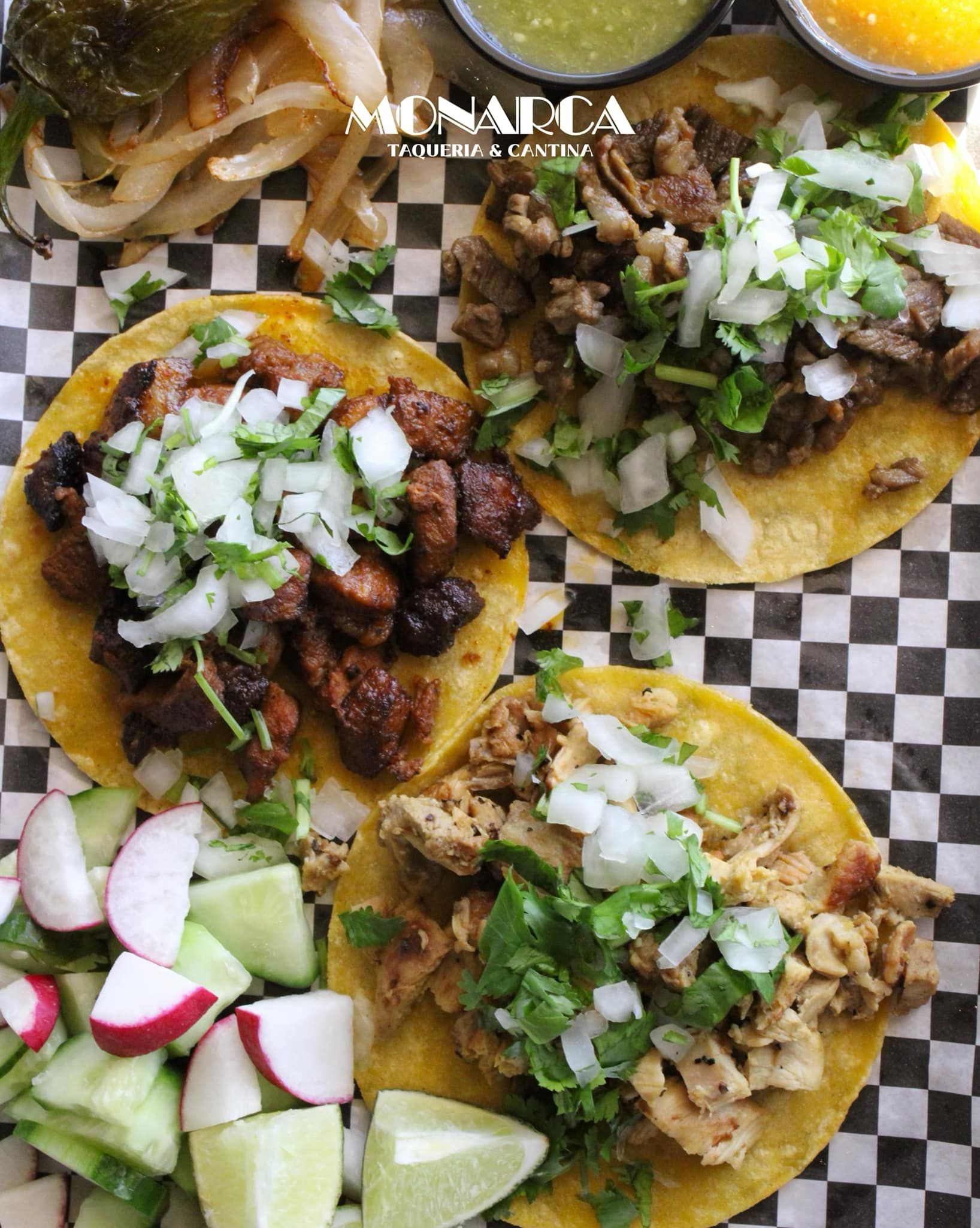 Three tacos are sitting on a checkered paper on a table.