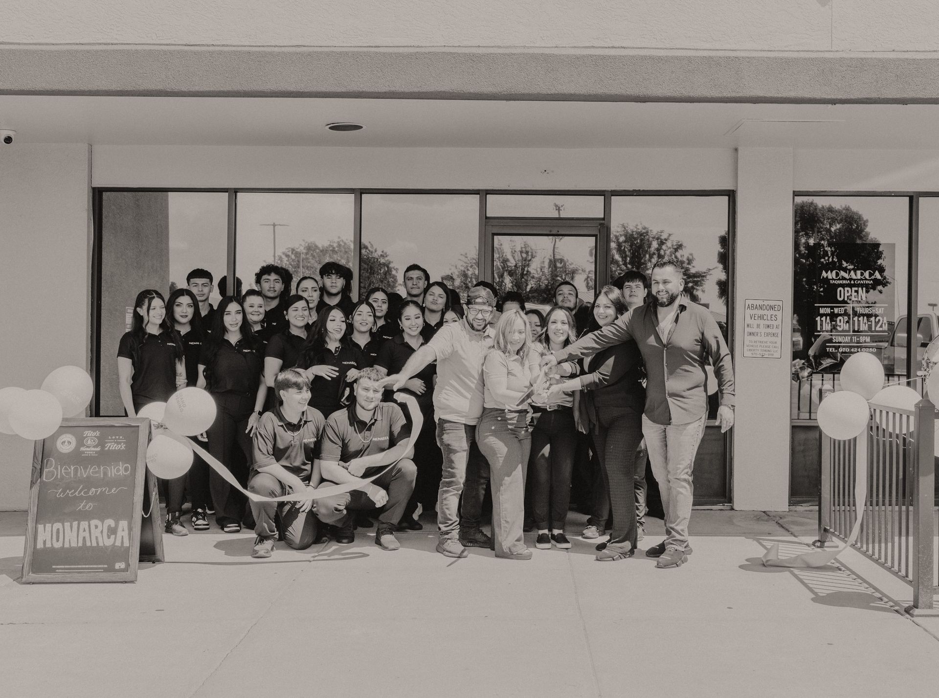 A group of people are standing in front of a building holding a ribbon.