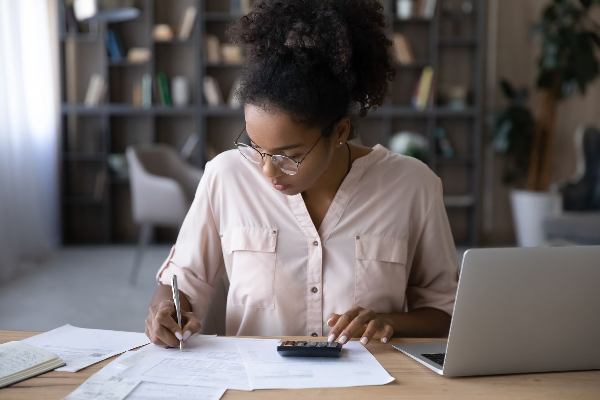 A woman is sitting at a desk with a laptop and a calculator.