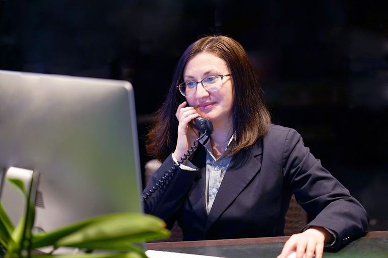 Woman in a dark suit wearing glasses, talking on the phone.
